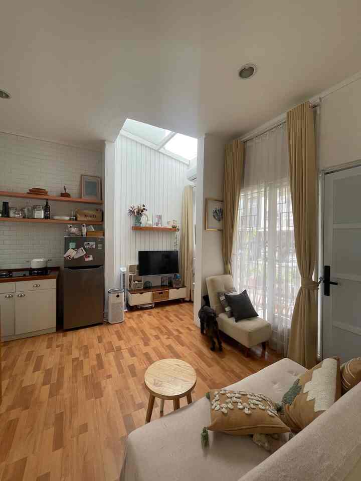 White walls and high ceiling with skylight, wood tone floor, beige curtains and sofa in a small living room and kitchen space featuring a dog