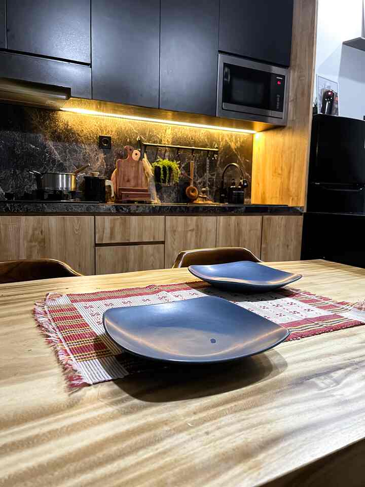 A warm kitchen space blending black and wood tones, featuring a dining table with blue ceramic plates set for a cozy meal preparation