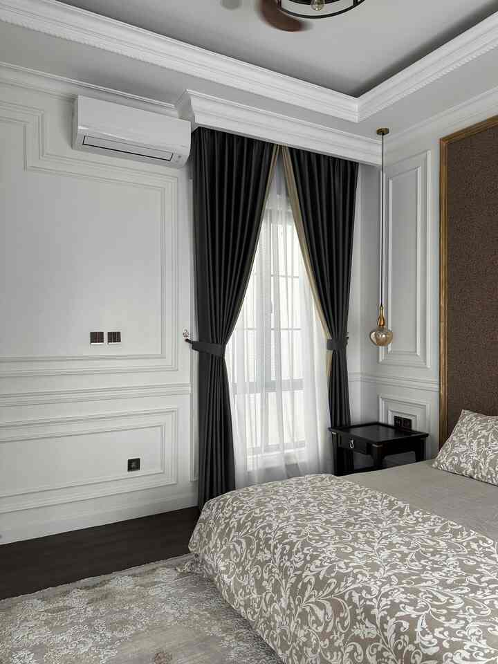 White and dark brown toned bedroom featuring classic molding and floor-to-ceiling blackout curtains with elegant atmosphere