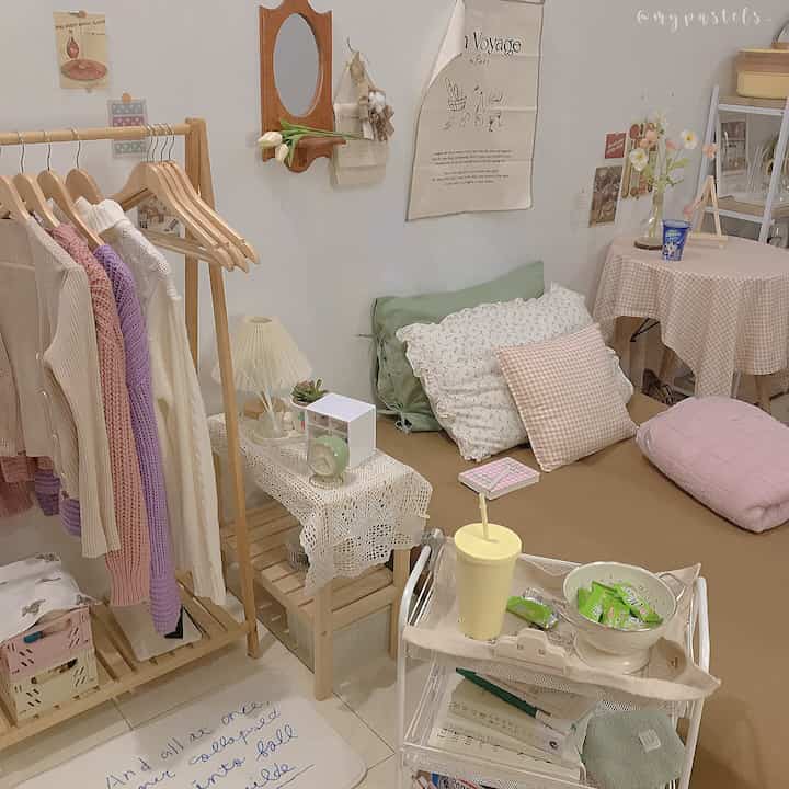 Pastel tones and white-walled studio bedroom featuring nightstand, clothing rack, and cushions in a cozy natural atmosphere