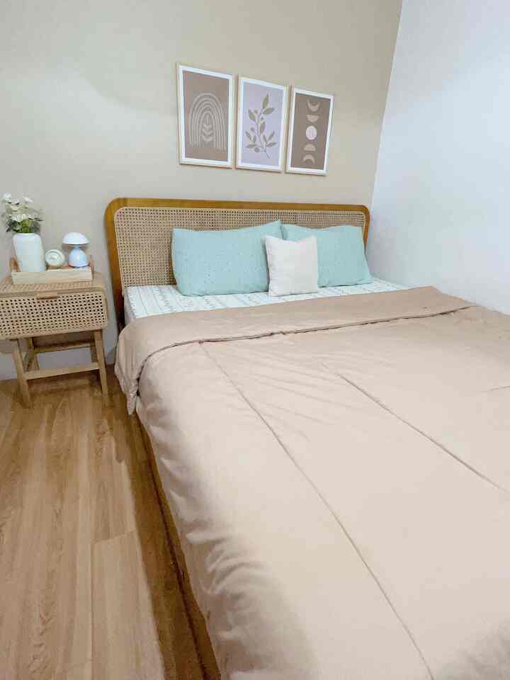 A simple bedroom in beige and light wood tones featuring a bed and nightstand creating a cozy atmosphere