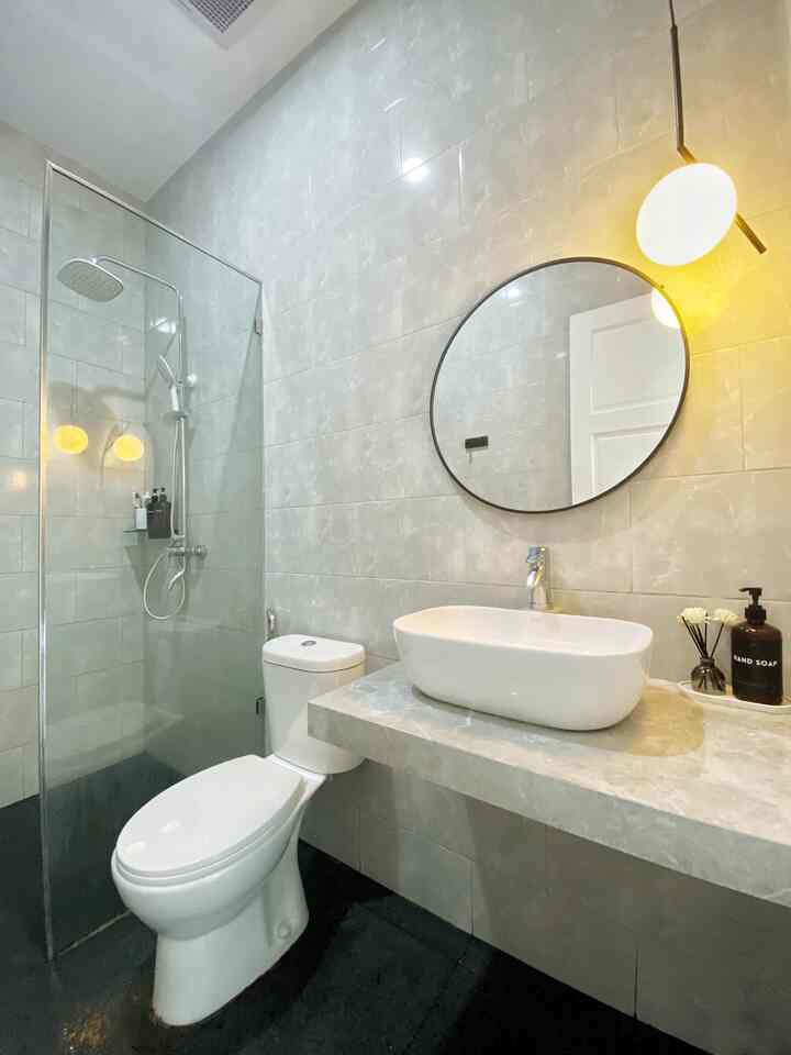 Modern small bathroom with gray tiles, white wash basin, and large round mirror creating a clean atmosphere
