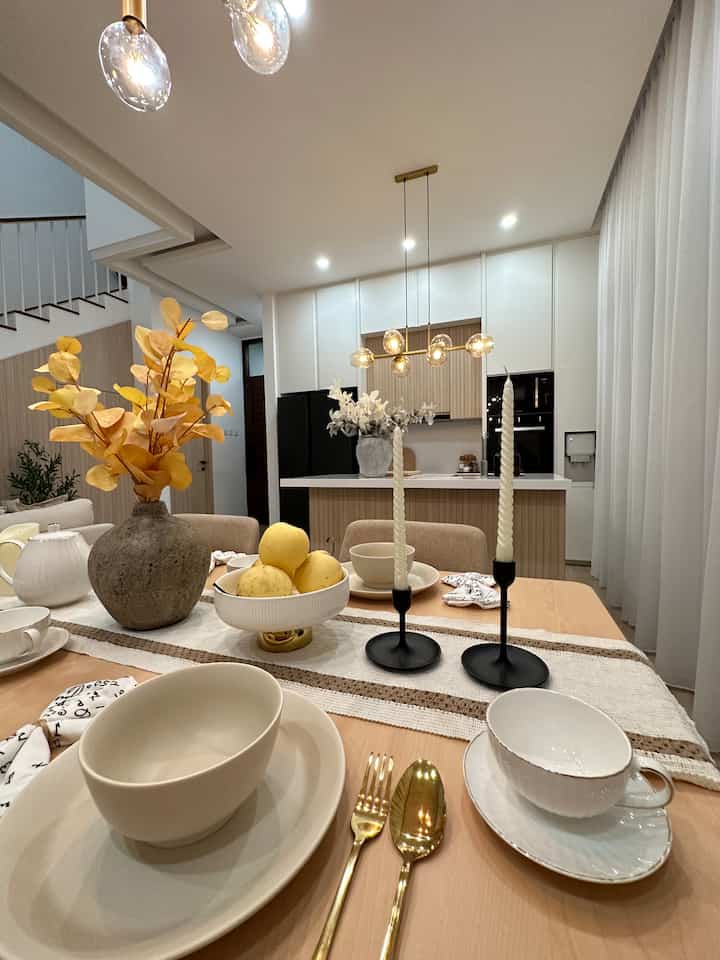 White and wood tone dining room and kitchen featuring a simple natural table setting with stylish lighting accents