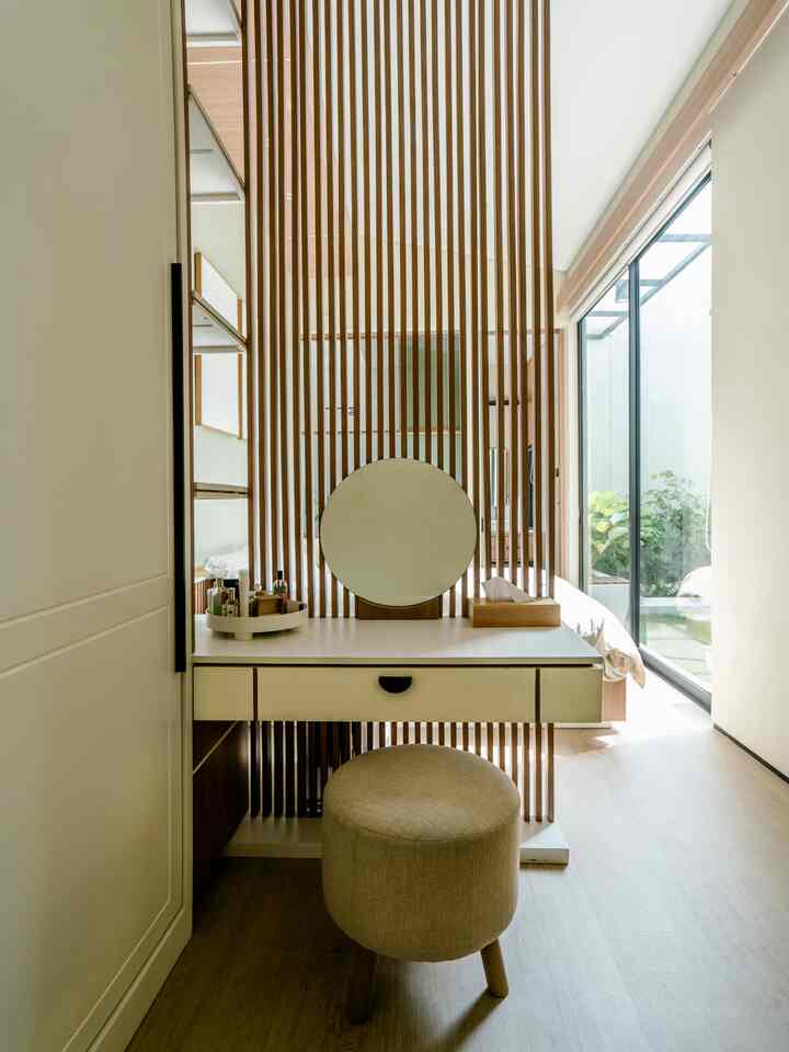 Bright white and wood-tone walk-in closet featuring wooden slat partition and vanity with stool in natural modern style