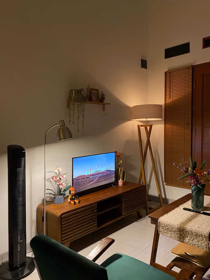 Living room with wood tones and white walls featuring a TV stand and floor lamp, creating a warm and natural atmosphere