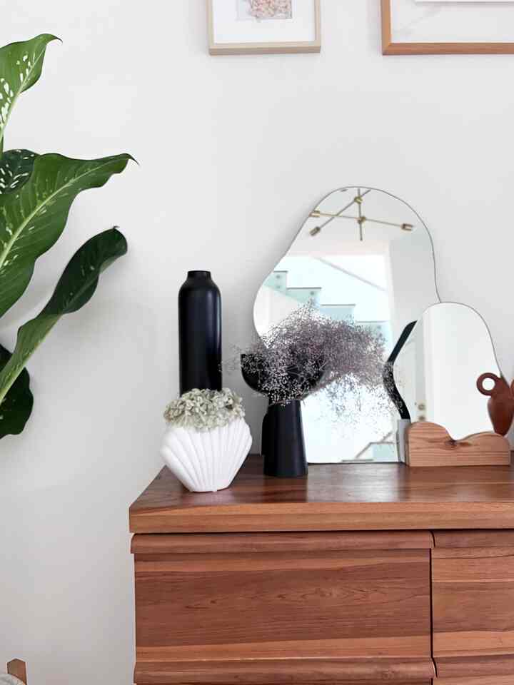 Natural-toned entrance space with console table featuring plant stands, vases, and uniquely shaped wall mirrors in a simple design