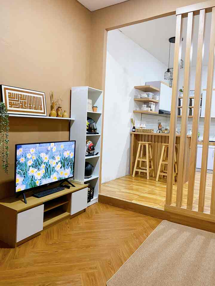 Wood tone flooring and brown accent wall in a small living room with open kitchen, featuring a TV stand and wooden stools in a cozy setting