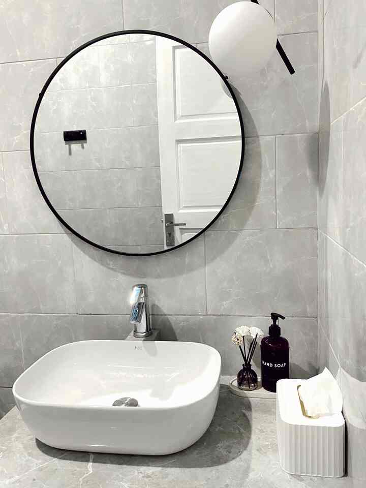 Modern bathroom with gray tiled walls, white sink, round black-framed mirror, and pendant light