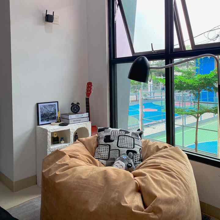 Simple cozy living room with beige bean bag and black lamp near a large window letting in natural light