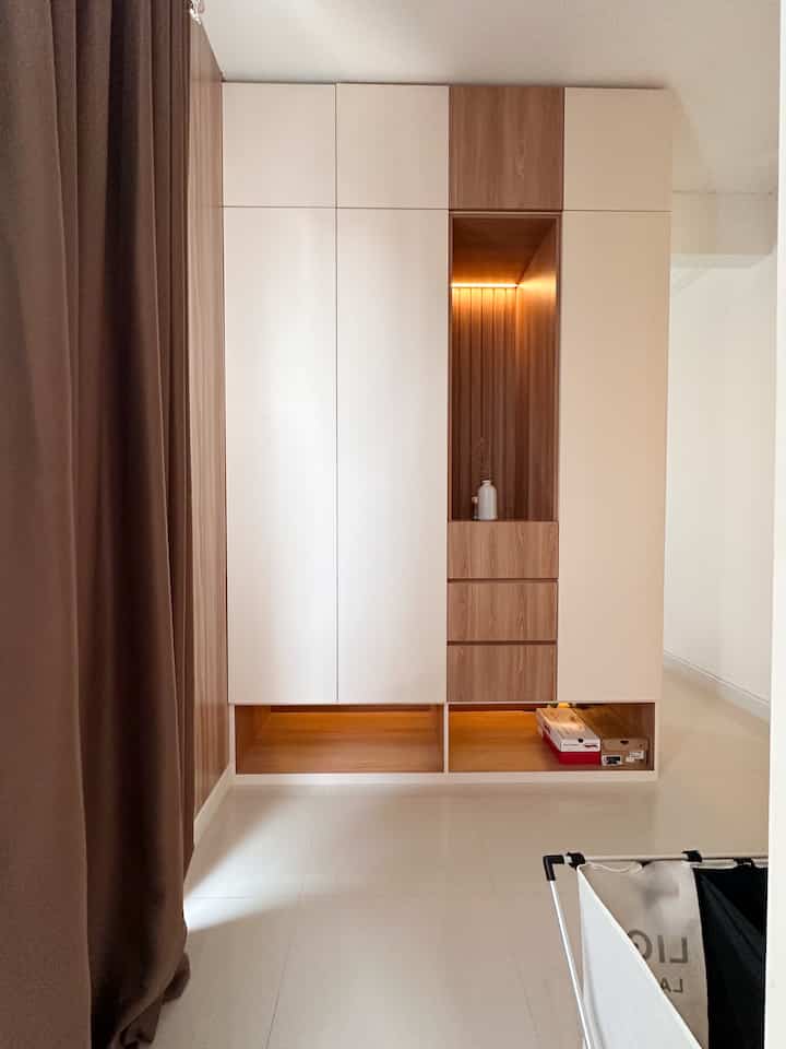 Modern walk-in closet with beige and wood tones, featuring simple wardrobe with central lighting and blackout curtain