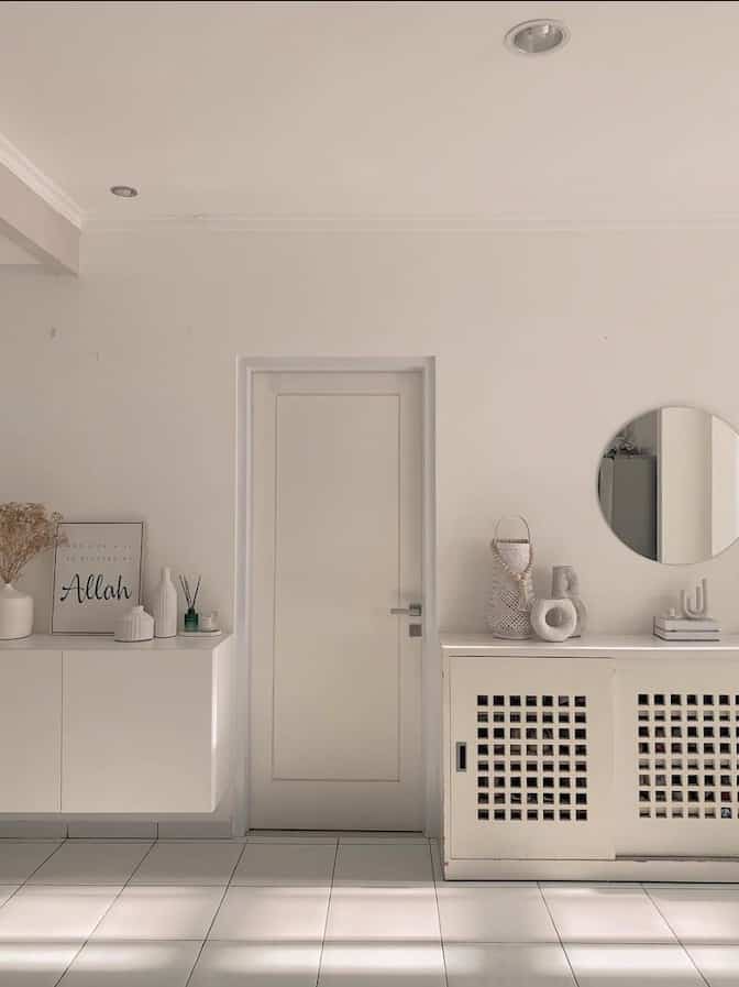 White and natural tone living room entrance space featuring cabinets, round mirror, and decor items with a clean, calm atmosphere