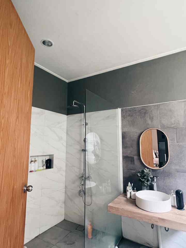 Modern bathroom with gray walls, marble tiles, a wooden door, and a vanity with a wooden mirror frame