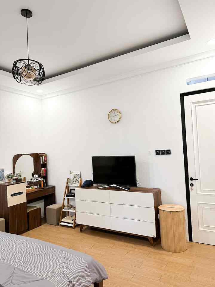 Modern compact bedroom with white walls and brown wood flooring featuring a vanity, dresser, and TV stand
