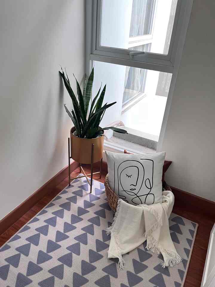 Natural tones of white and gray in a corner space featuring a plant by the window and an abstract face cushion, creating a cozy interior