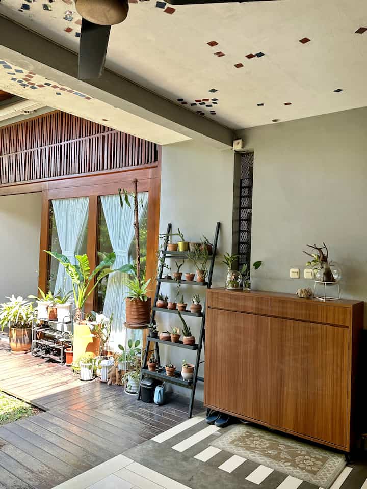 Natural color and wood tone entrance featuring multiple potted plants and wooden furniture with an open tropical garden view