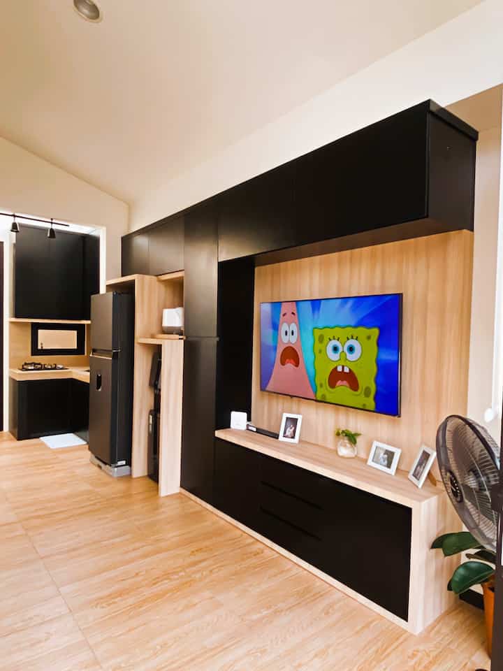 A modern living room and kitchen space with black and wood tones, featuring a TV and storage units