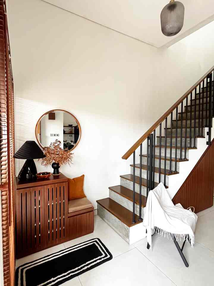 Modern entrance with white walls and wood-toned furniture, cozy atmosphere featuring storage cabinet under stairs and a stool