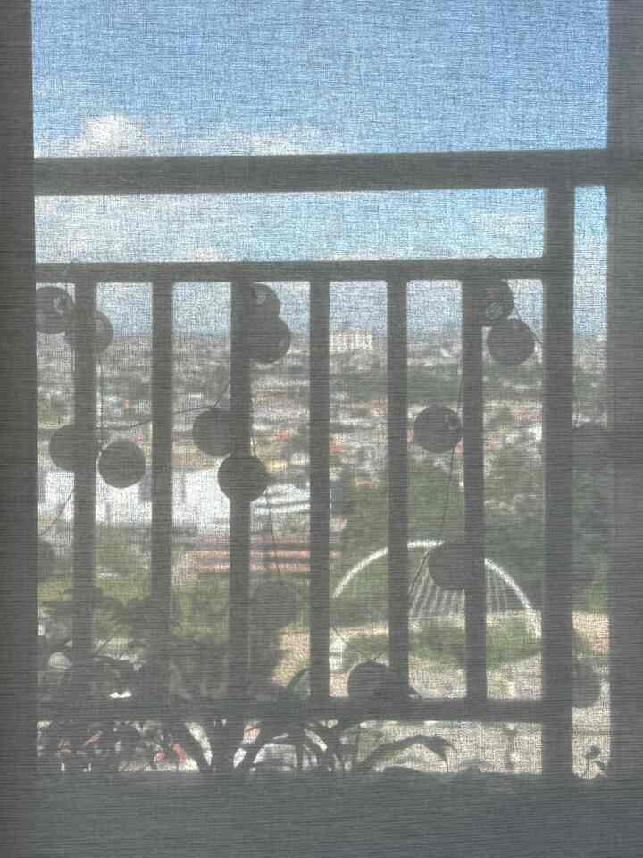 Natural-lit studio apartment balcony featuring string lights hung on railing with soft curtain filtering daylight