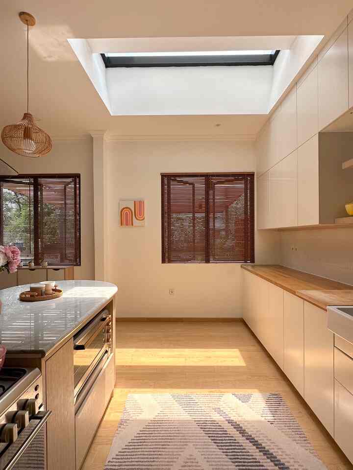 Bright and cozy kitchen with white walls and natural wood tones, featuring a central skylight and brown blinds