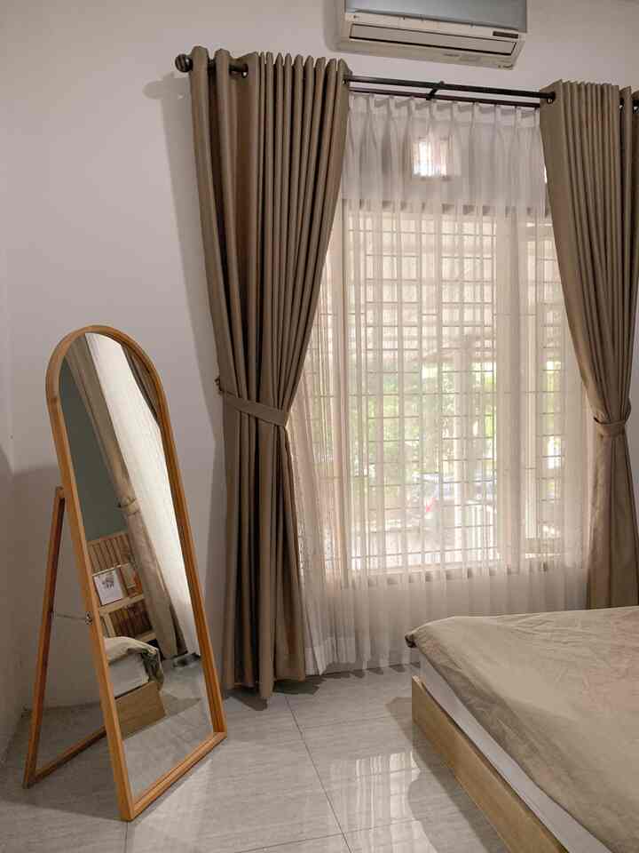 Beige and white toned bedroom featuring large window and wooden frame mirror with cozy natural atmosphere