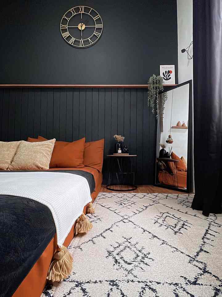 Minimal bedroom with black wall batten and brown leather bed, featuring warm-toned carpet and white duvet cover accents
