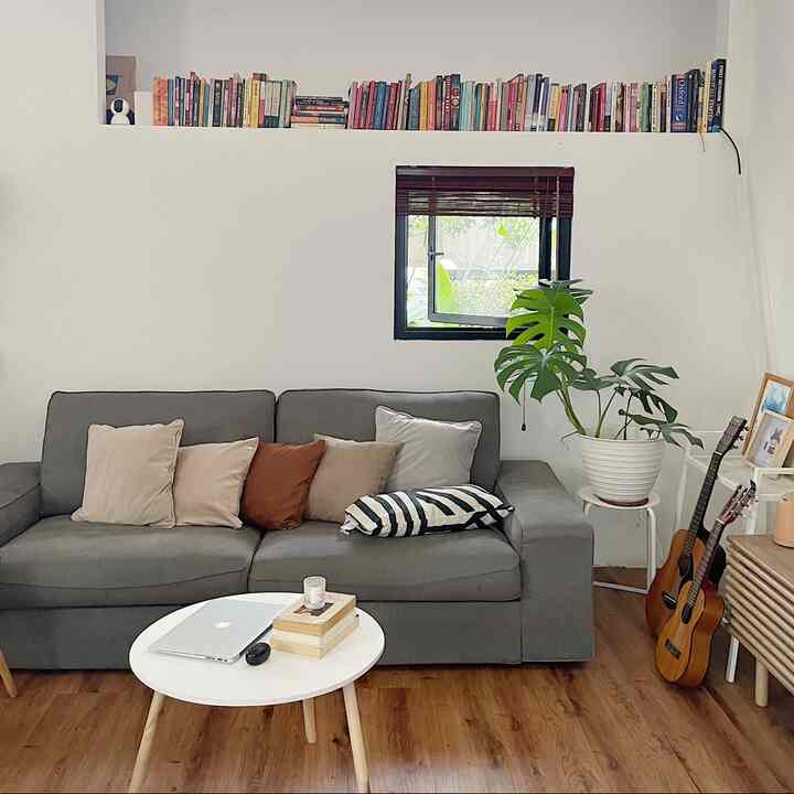 Natural modern living room with gray sofa, wooden floor, and wall-mounted bookshelf filled with books