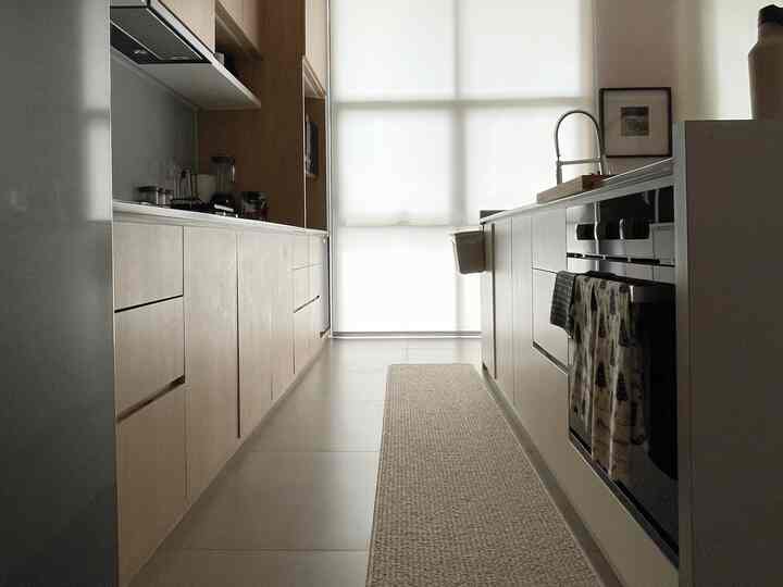 A narrow kitchen in beige and natural tones featuring wood cabinetry on both sides, creating a neat space