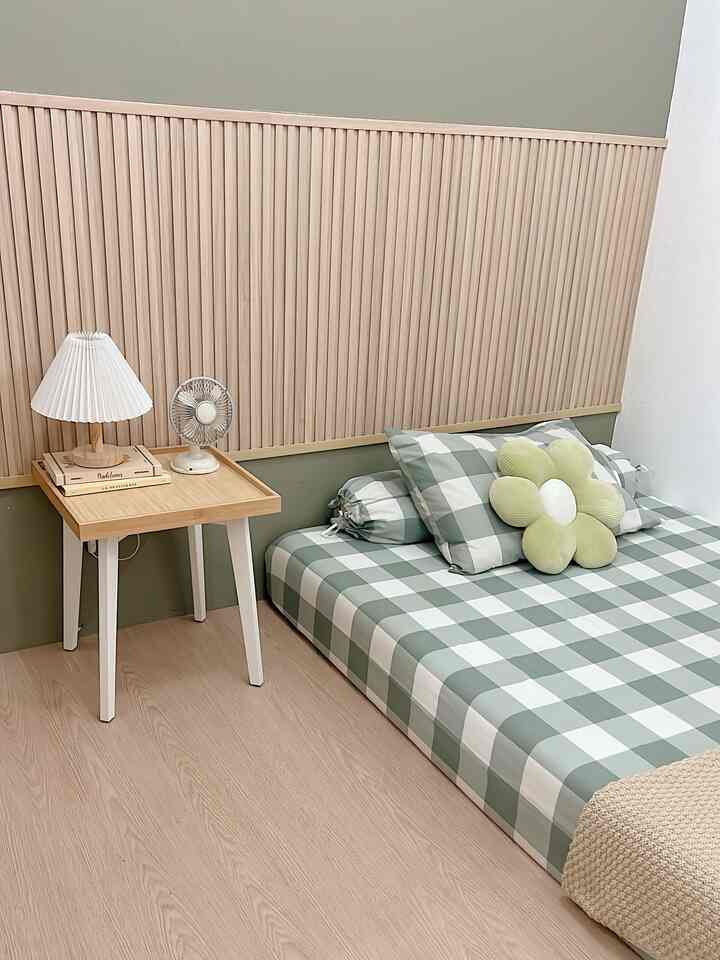 Natural tones bedroom with green painted wall and wood paneling, checkered bedding and flower-shaped cushion create cozy kids' room atmosphere