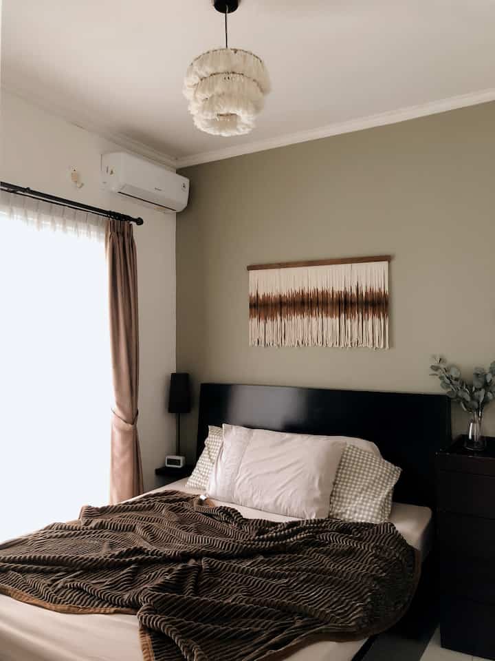 Beige-walled small 3x3m bedroom with brown bedding, macrame decor, and plants creating a cozy atmosphere
