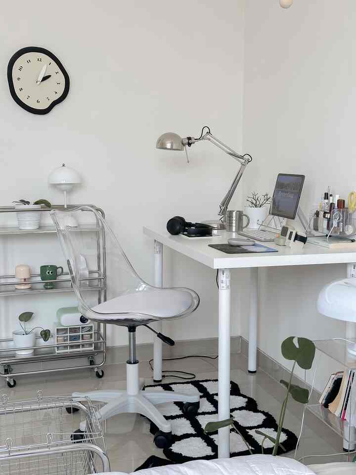 Bright white-walled home office with transparent office chair, black-and-white patterned carpet, and plants on desk creating a cozy atmosphere.