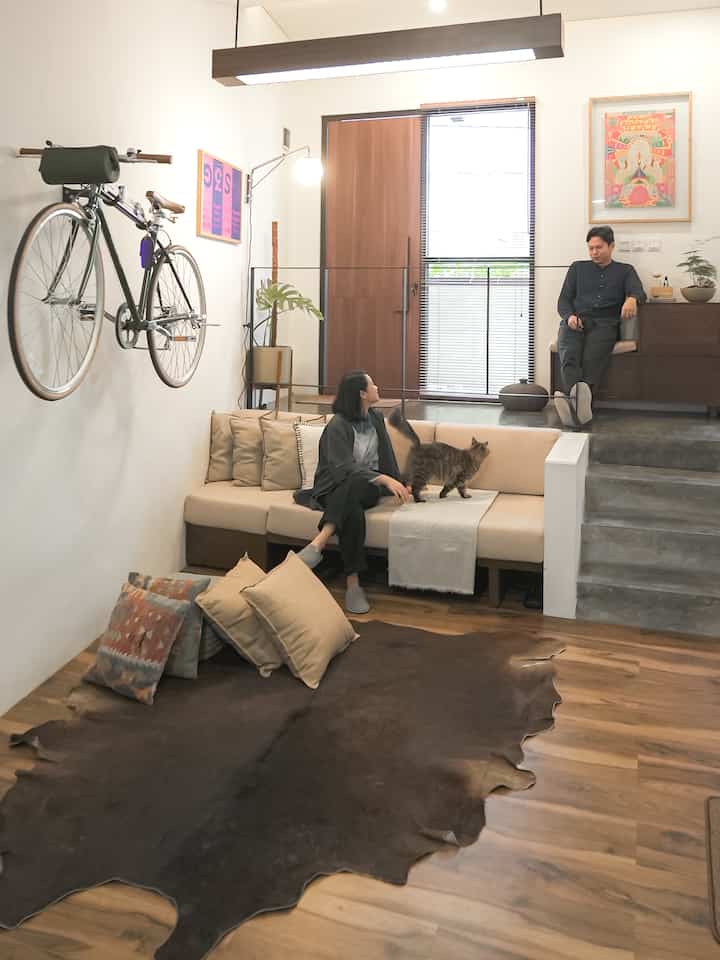 Beige sofa and wood tone floor in Asian-style compact living room, two people seated with a cat in a cozy setting