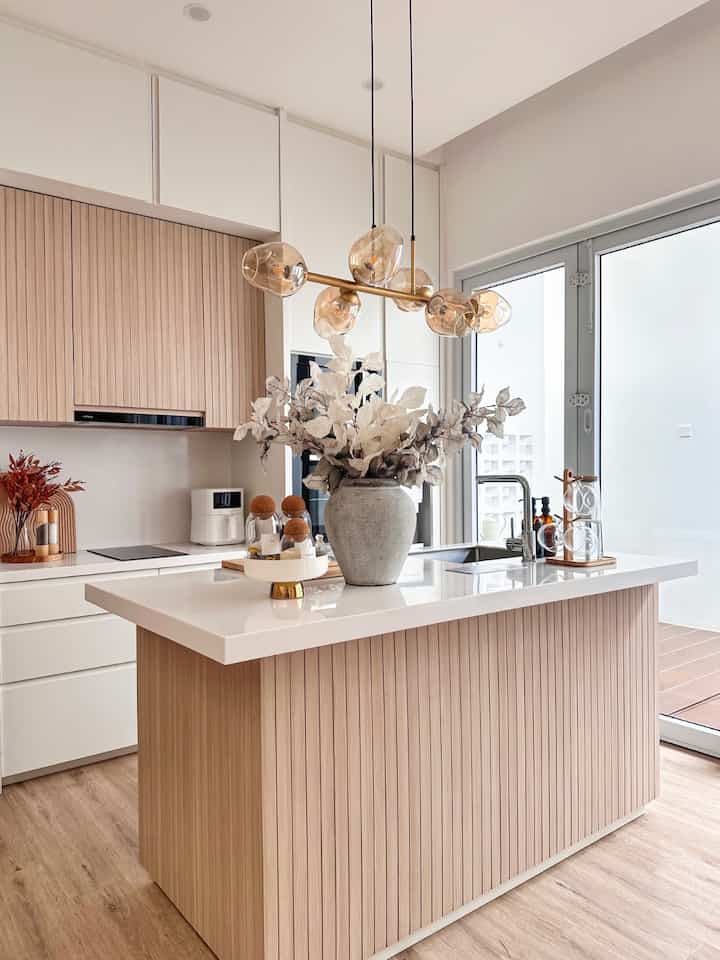 Modern Japandi kitchen in white and wood tones featuring a central island and pendant lighting, creating a warm open space