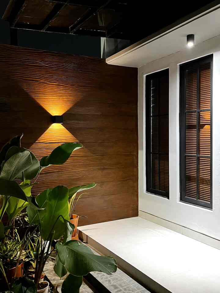 Minimal house entrance exterior with warm wood-tone wall and white tiled floor, softly lit by wall sconces at night