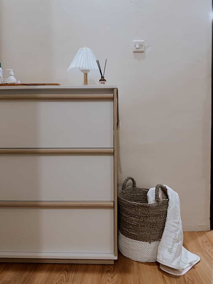 Simple storage space with a bright white 3-drawer dresser and natural wood-tone basket harmonizing warmly