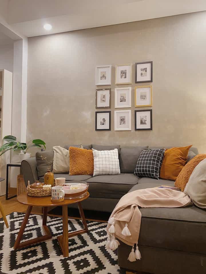 Cozy living room in warm brown and gray tones featuring a gray sectional sofa, round coffee table, multiple cushions, and framed pictures