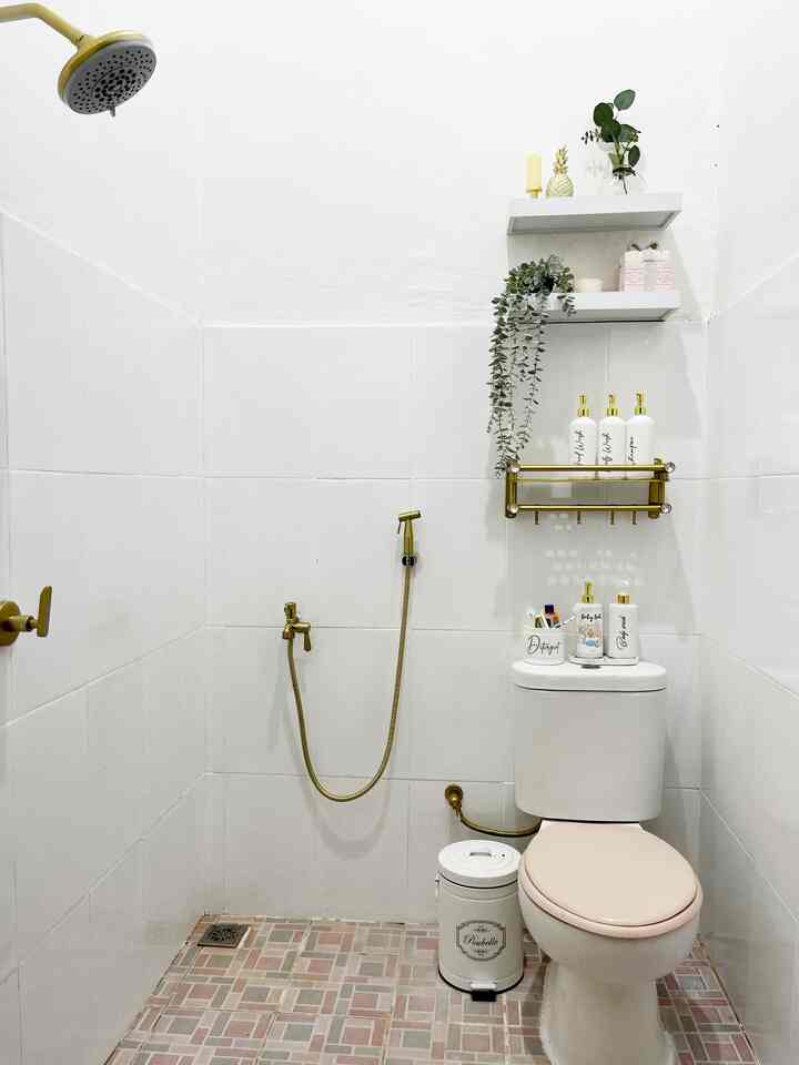 White and gold toned small compact bathroom featuring a toilet, gold fixtures, storage shelves, and a trash bin with a neat atmosphere