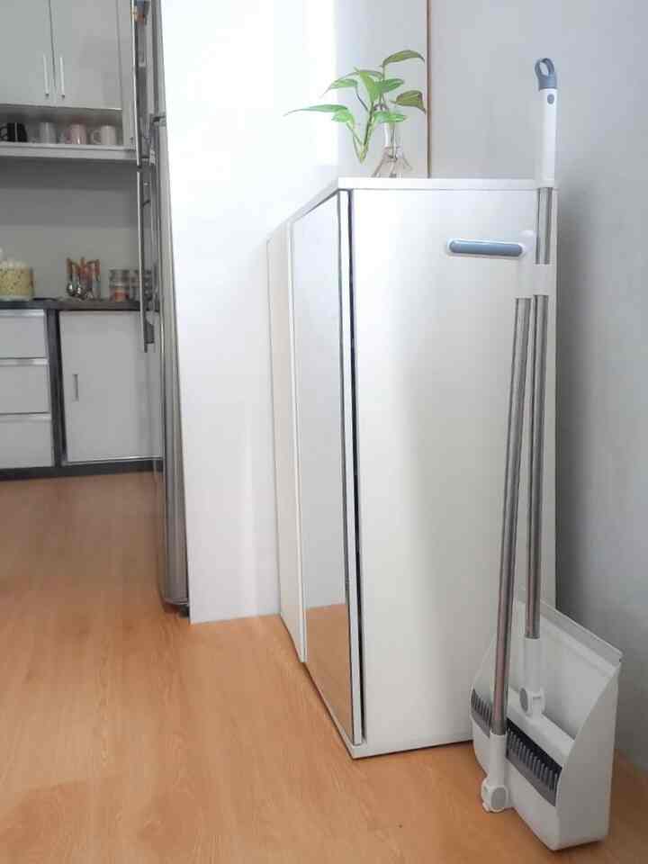 Minimal space next to kitchen featuring white shoe cabinet and cleaning tools with wood tone flooring