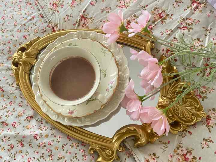 Cozy bedroom scene with floral bedding and pink flowers on an ornate gold vintage mirror tray centerpiece.