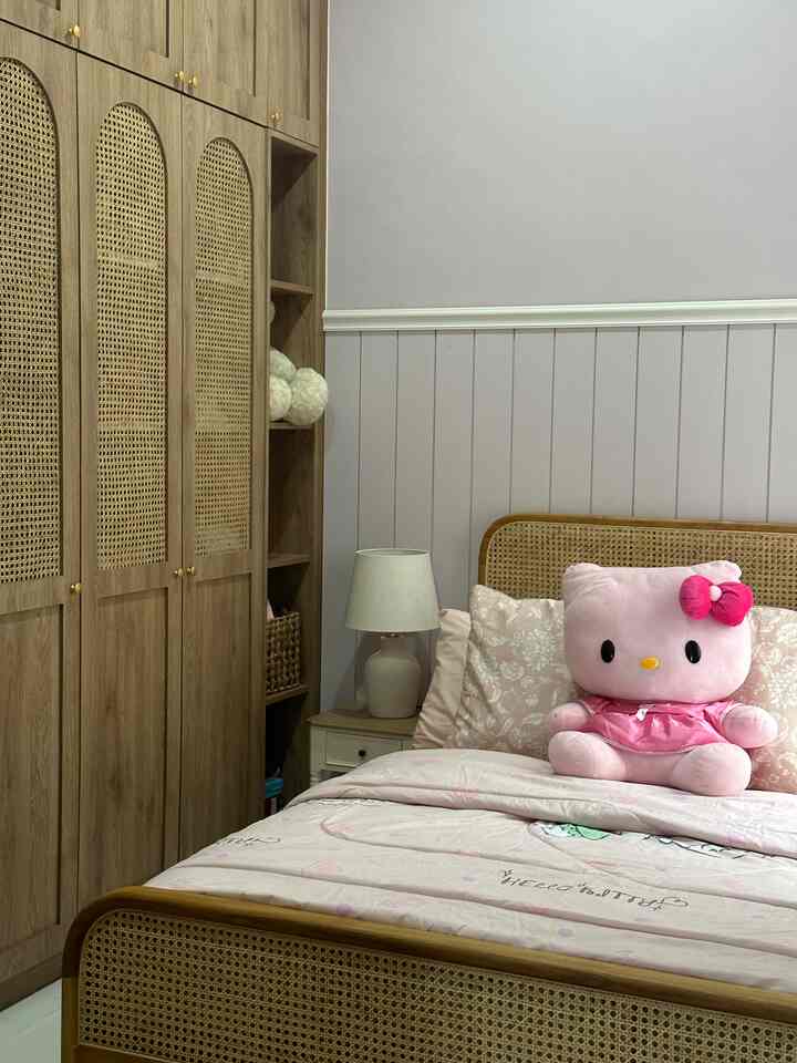 Wood tone and white themed bedroom featuring rattan furniture and a large pink Hello Kitty plush toy in a cozy kids' room