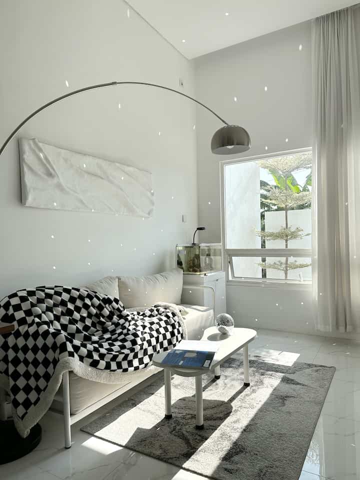 Bright white living room featuring black-and-white checkered blanket, natural light streaming through window in modern clean space