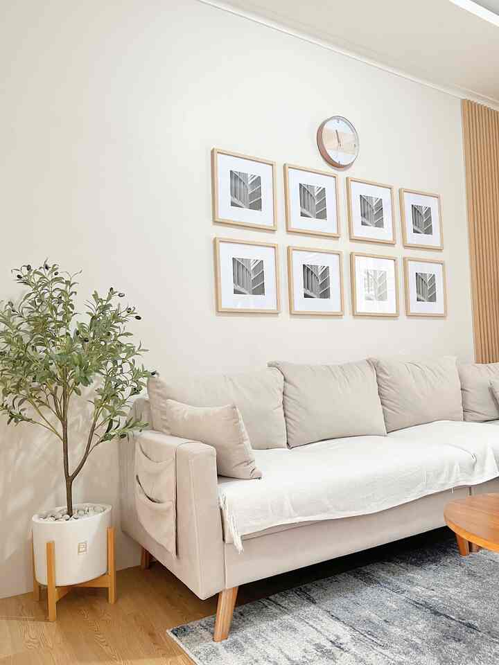 Beige and wood-toned living room featuring a beige sofa, wooden picture frames, and an artificial olive tree in a clean Japandi style space