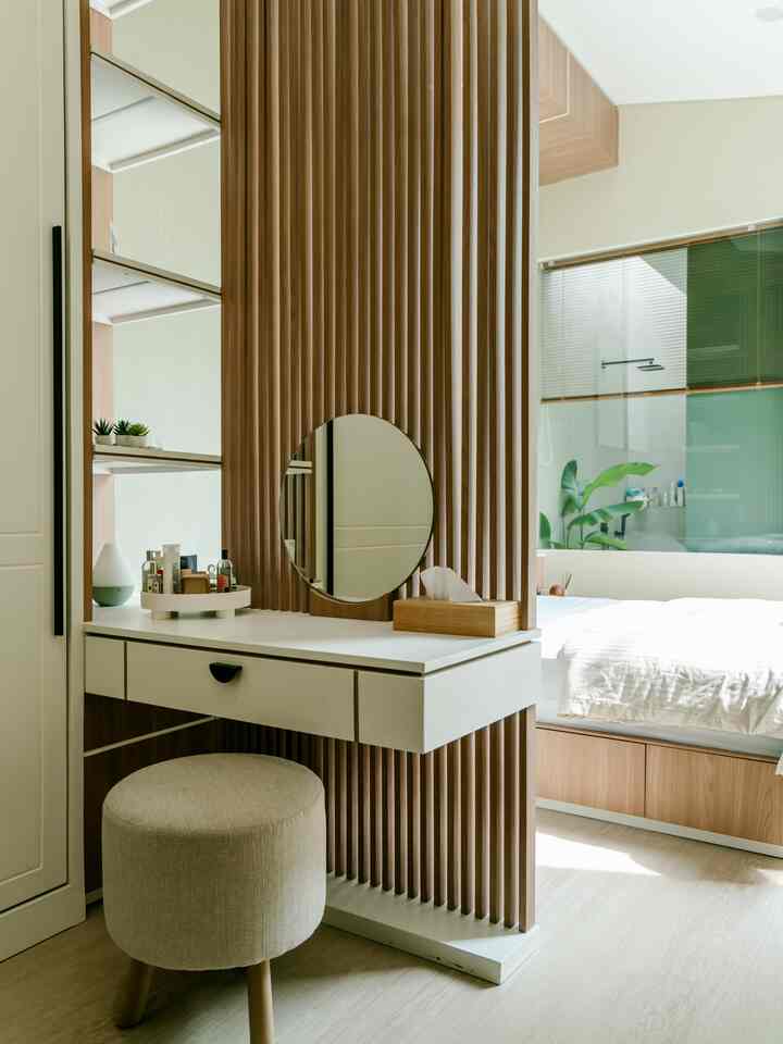 A cozy walk-in closet and bedroom space combining white and wood tones, featuring a vanity with a round mirror.