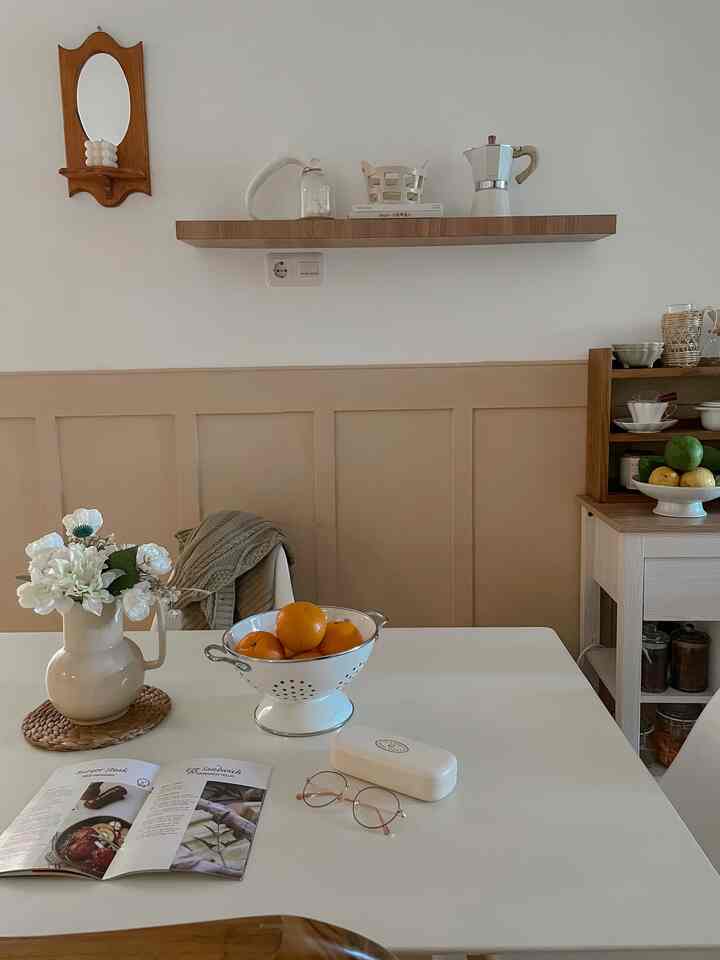 White and beige toned kitchen and dining area with oranges and floral decoration creating a cozy cafe style vibe