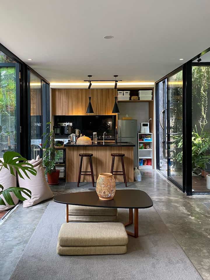 Modern open living and kitchen space featuring white ceilings, black accents, natural wood tones, and large glass windows.