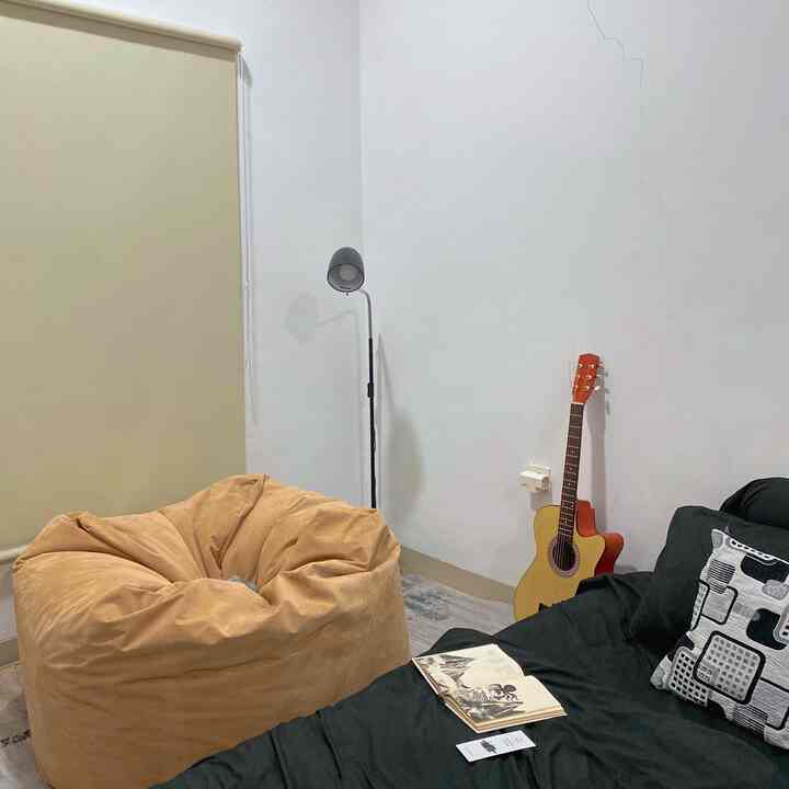 A beige and black toned bedroom featuring a bean bag, bed, and guitar creating a cozy chill-out zone