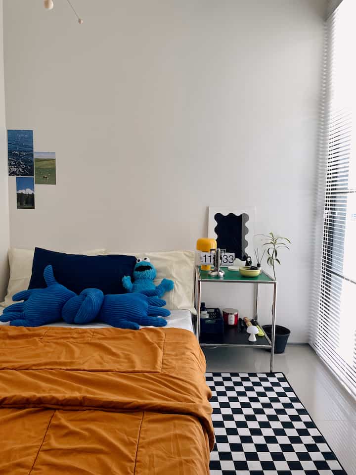White-walled bedroom with orange bedding and blue cushions and plush toys, styled in Mid-Century Modern decor