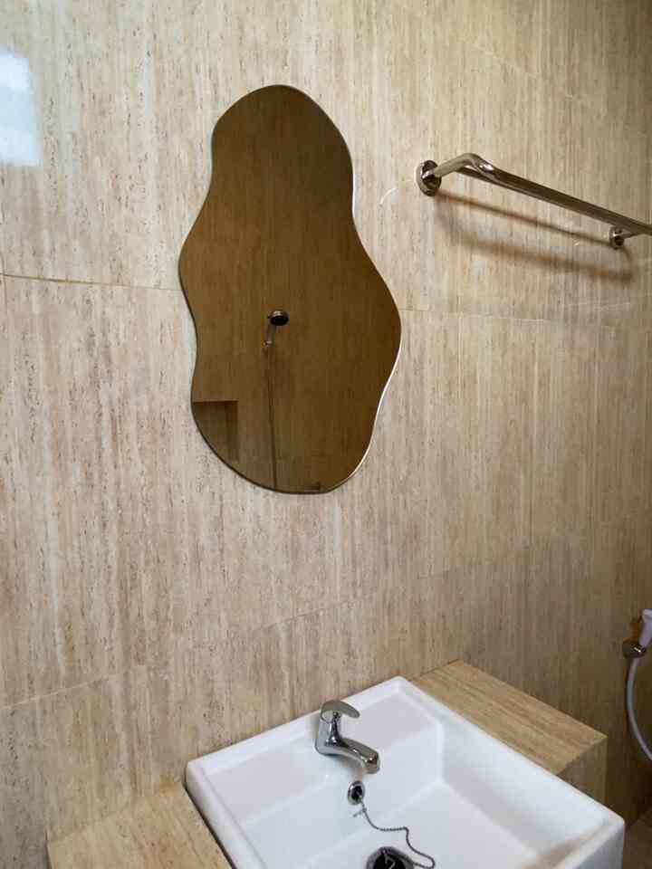 Warm brown-toned bathroom featuring an irregularly shaped mirror and white sink creating a cozy atmosphere