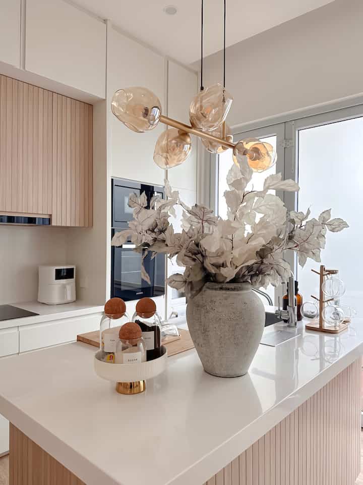 White and wood-toned Japandi kitchen featuring pendant lights and a large vase, creating a modern atmosphere