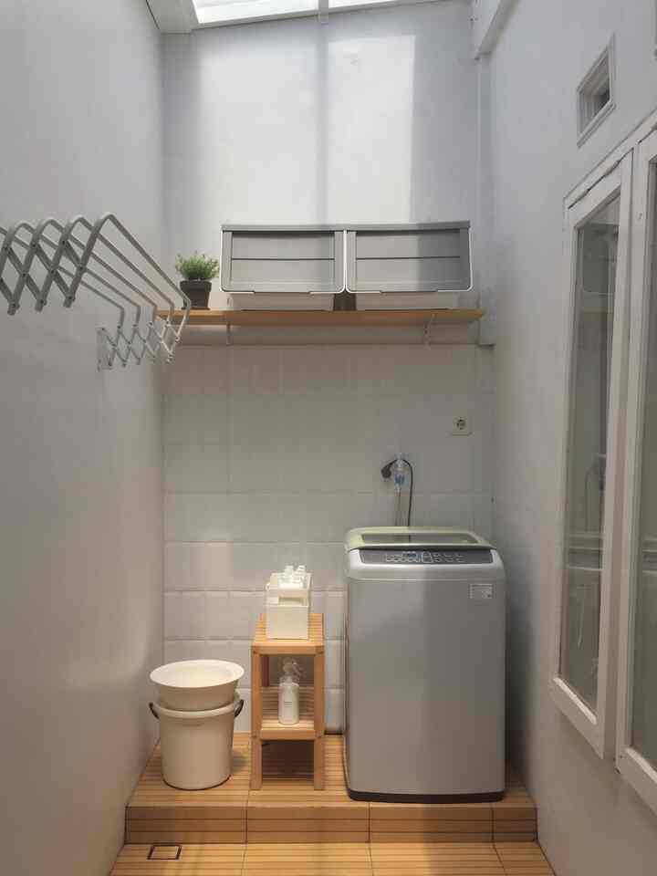 White and wood-tone long narrow laundry room featuring washing machine, storage shelves, and wall tiles in a clean layout