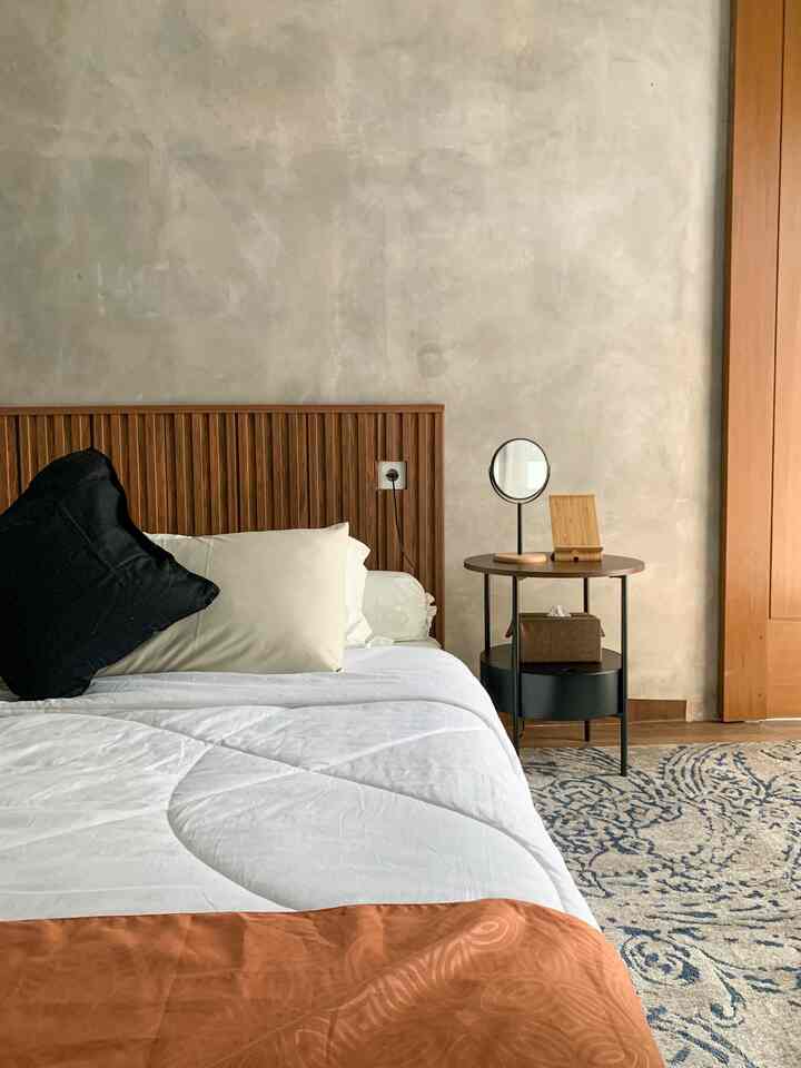 Natural brown and white toned bedroom featuring wood nightstand and round mirror with a simple and cozy atmosphere